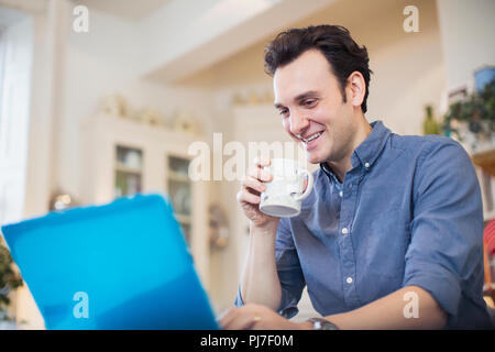 Smiling man drinking coffee, working at laptop Stock Photo