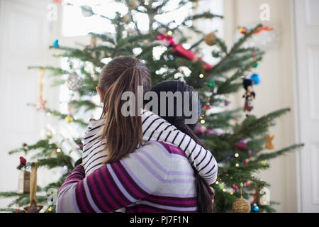 Affectionate mother and daughter hugging in front of Christmas tree Stock Photo