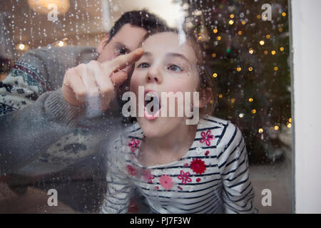 Playful father and daughter drawing in condensation on wet winter window Stock Photo