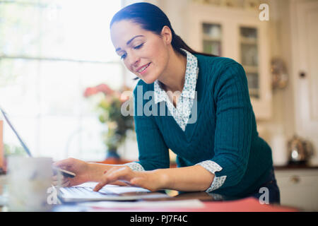 Woman using laptop in kitchen Stock Photo