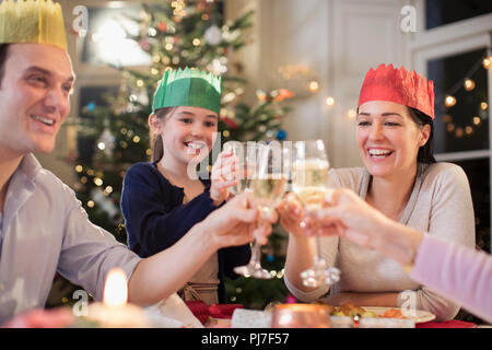 Happy family in paper crows toasting water and champagne glasses at Christmas dinner Stock Photo