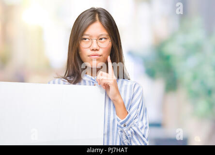 Young asian woman over isolated background holding blank banner serious face thinking about question, very confused idea Stock Photo