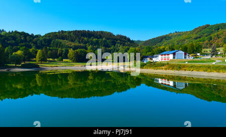 Symmetrical reflection of a forest and a building, Rursee, Germany Stock Photo