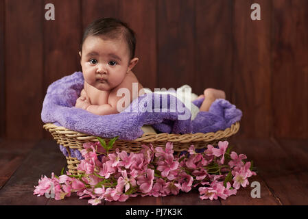 Baby girl lay in basket look to camera on dark wooden background Stock Photo