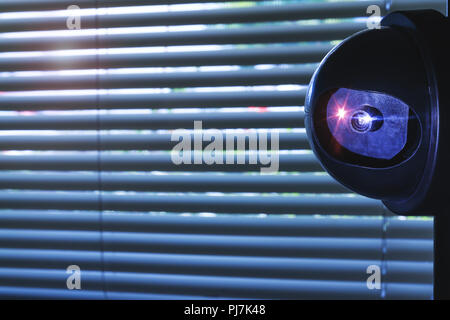 Security Camera inside of the office building or home room, in front of the window blinds. CCTV camera or surveillance system installed on wall. Priva Stock Photo
