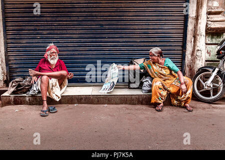 Senior citizen woman reading newspaper and senior citizen man sitting nearby. The photo was taken in Summer in city of Ahmedabad Stock Photo