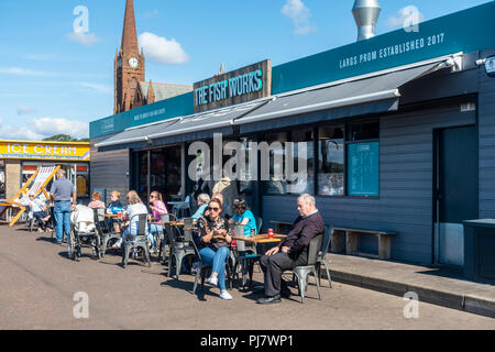 Customers eating and drinking outside The Fish Works, a fish and chips shop on Largs Promenade, North Ayrshire, on a sunny early September day. Stock Photo