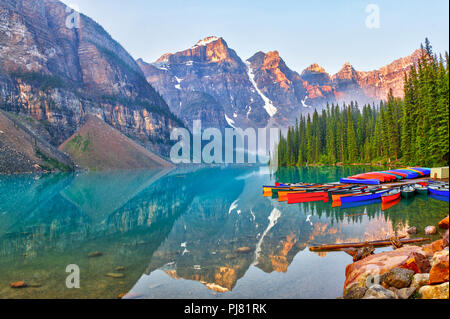 Sunrise over the Valley of the Ten Peaks with canoes on the glacier-fed, turquoise colored Moraine Lake in the Canadian Rockies. Stock Photo