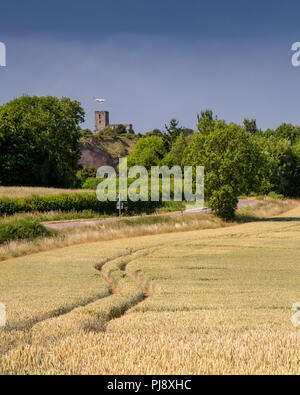 Breedon, England, UK - July 3, 2018: An aeroplane on the approach to landing at East Midlands Airport passes behind the hilltop Priory Church of Breed Stock Photo