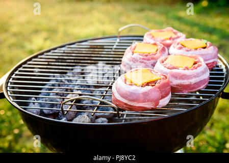 Making home made Beer Can Bacon Burgers on barbecue grill. Preparing stuffed patties, wrapped  in bacon and grilling on indirect heat in nature at bac Stock Photo