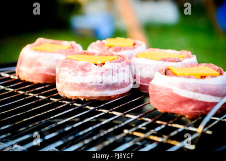 Making home made Beer Can Bacon Burgers on barbecue grill. Preparing stuffed patties, wrapped  in bacon and grilling on indirect heat in nature at bac Stock Photo