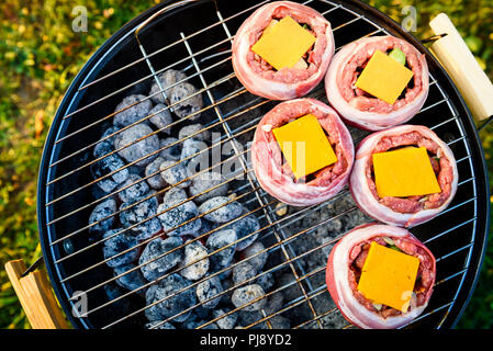 Making home made Beer Can Bacon Burgers on barbecue grill. Preparing stuffed patties, wrapped  in bacon and grilling on indirect heat in nature at bac Stock Photo