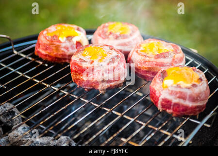 Making home made Beer Can Bacon Burgers on barbecue grill. Preparing stuffed patties, wrapped  in bacon and grilling on indirect heat in nature at bac Stock Photo