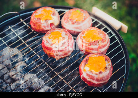 Making home made Beer Can Bacon Burgers on barbecue grill. Preparing stuffed patties, wrapped  in bacon and grilling on indirect heat in nature at bac Stock Photo