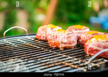 Making home made Beer Can Bacon Burgers on barbecue grill. Preparing stuffed patties, wrapped  in bacon and grilling on indirect heat in nature at bac Stock Photo