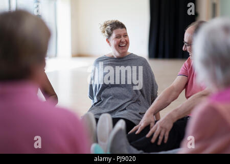 Laughing instructor and active seniors stretching legs in exercise class Stock Photo