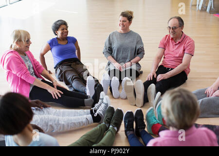 Instructor and active seniors stretching legs in circle in exercise class Stock Photo