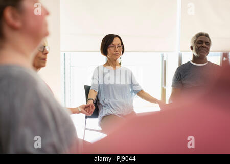 Serene active seniors holding hands and meditating in community center Stock Photo