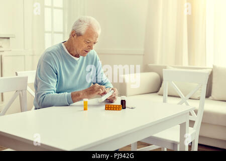 Lonely retired man taking medication out of weekly organizer Stock Photo