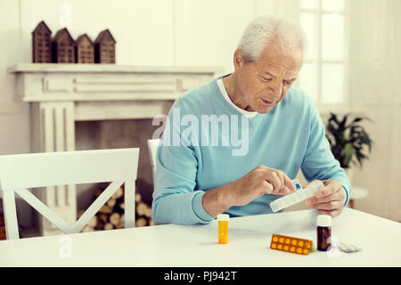 Retired man sitting at table and taking medication Stock Photo