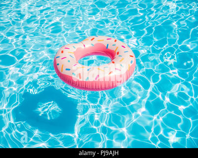 Pink inflatable donut swimming ring in a swimming pool Stock Photo