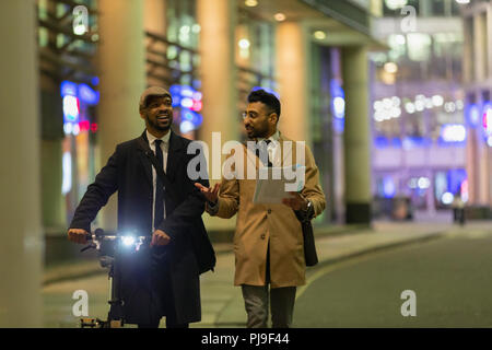 Businessmen talking, discussing paperwork on urban sidewalk at night Stock Photo
