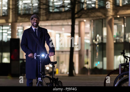 Portrait confident businessman with bicycle on urban street at night Stock Photo