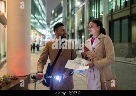 Business people discussing paperwork on urban sidewalk at night Stock Photo