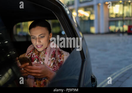 Businesswoman using smart phone in crowdsourced taxi at night Stock Photo
