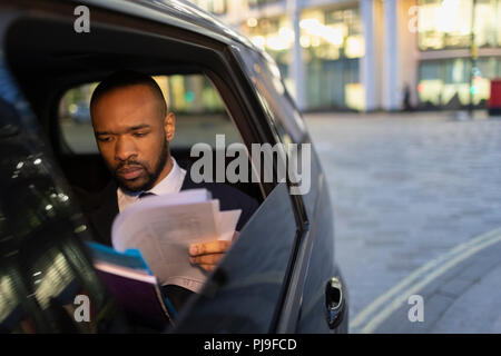 Businessman reading paperwork in crowdsourced taxi at night Stock Photo