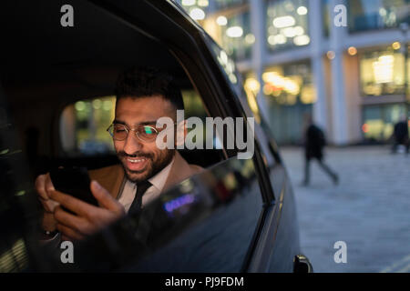 Businessman using smart phone in crowdsourced taxi at night Stock Photo