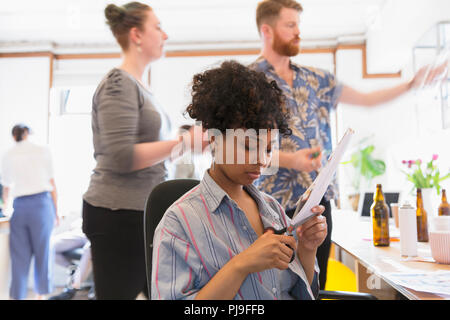 Creative female designer cutting photograph in office Stock Photo