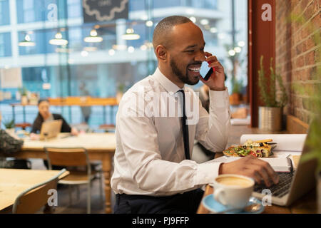 Smiling businessman talking on smart phone, working in cafe Stock Photo