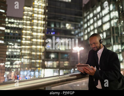 Businessman with headphones using digital tablet on urban pedestrian bridge at night Stock Photo