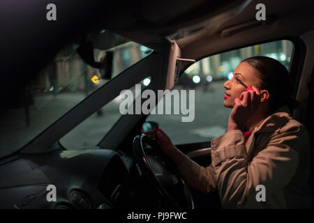 Businesswoman applying mascara in car at night Stock Photo
