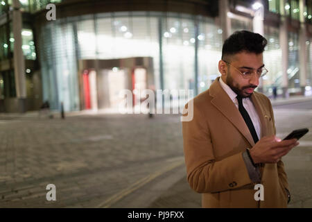 Businessman texting with smart phone on urban street corner at night Stock Photo