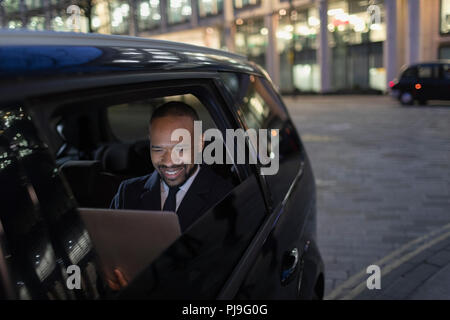 Smiling businessman using laptop in crowdsourced taxi at night Stock Photo