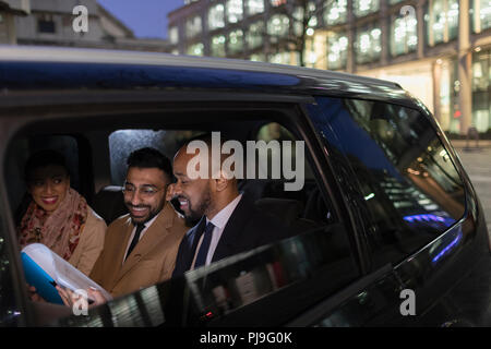 Business people reviewing paperwork in crowdsourced taxi at night Stock Photo