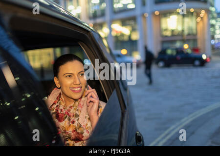 Smiling businesswoman talking on smart phone in crowdsourced taxi at night Stock Photo