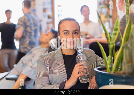 Portrait confident businesswoman drinking bottled water in office Stock Photo