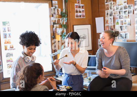 Creative female designers eating sushi in office Stock Photo