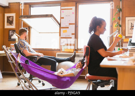 Creative female designer with dog napping in hammock in office Stock Photo