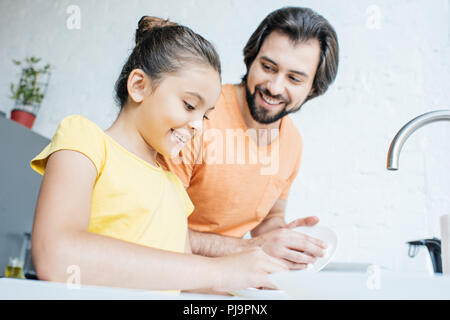 father and daughter washing dishes together at home Stock Photo
