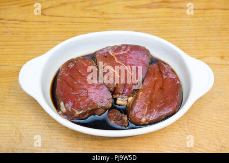 Beef steak eye fillet - lean meat with minimal fat - marinading in white dish of soy sauce on wooden background with copy space Stock Photo