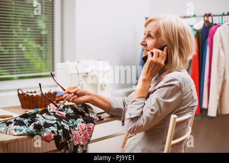 Adult woman is sewing in her studio. She is talking to client. Stock Photo