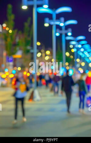 Abstract bright blurred background with bright bokeh, city street in  evening, unidentified people, defocused motion. Vivid illumination, shop  windows and street lamps. Concept of seasons, modern city, urban lifestyle,  leisure Stock Photo -