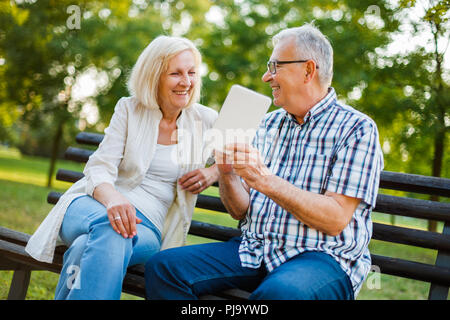 Happy senior couple is using digital tablet in park. Stock Photo