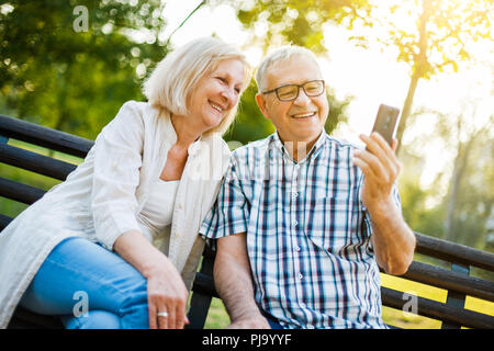 Happy senior couple is using smartphone in park. Stock Photo