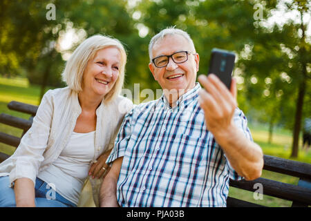 Happy senior couple is using smartphone in park. Stock Photo