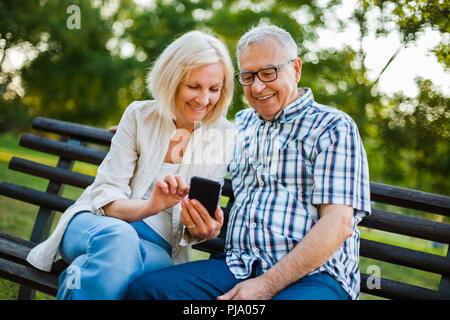 Happy senior couple is using smartphone in park. Stock Photo